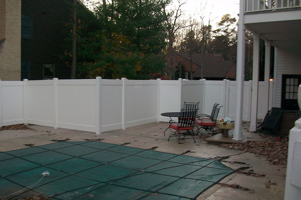 White vinyl fence encloses a patio with pool cover, table, chairs, and house in background.