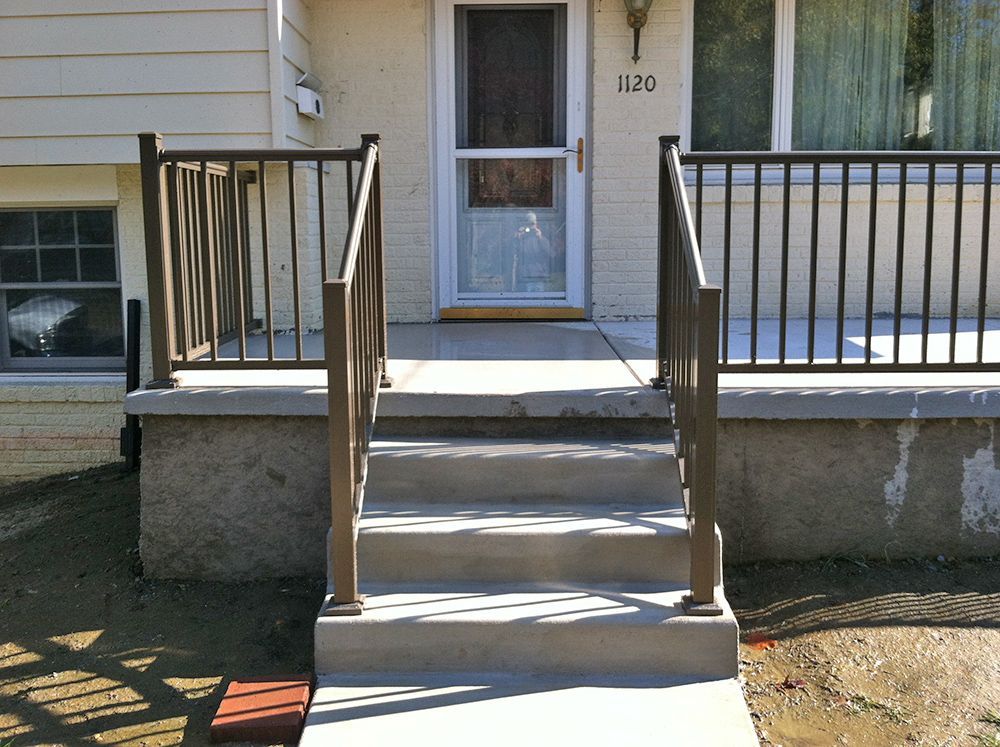 Brown handrails on concrete steps leading to a house with a screen door.