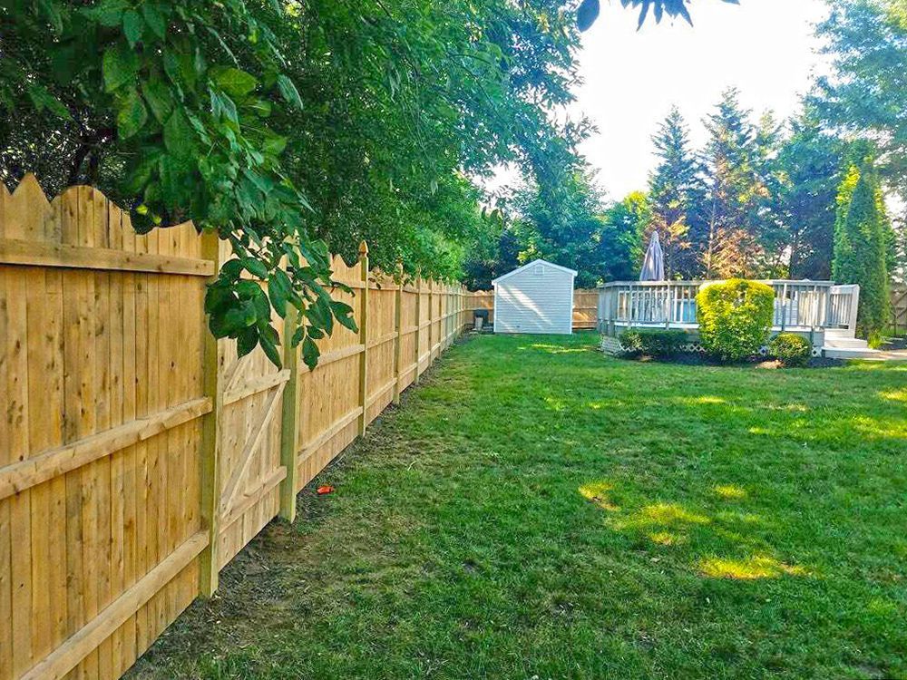Wooden fence in a backyard with green grass, a shed, and a pool in the distance.