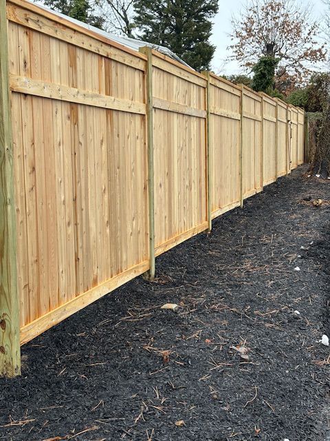 Wooden fence along a dark gravel path. The fence is made of light-colored wood.