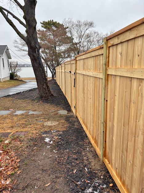 Wooden fence curves along a shoreline. A gate is visible. Overcast sky.