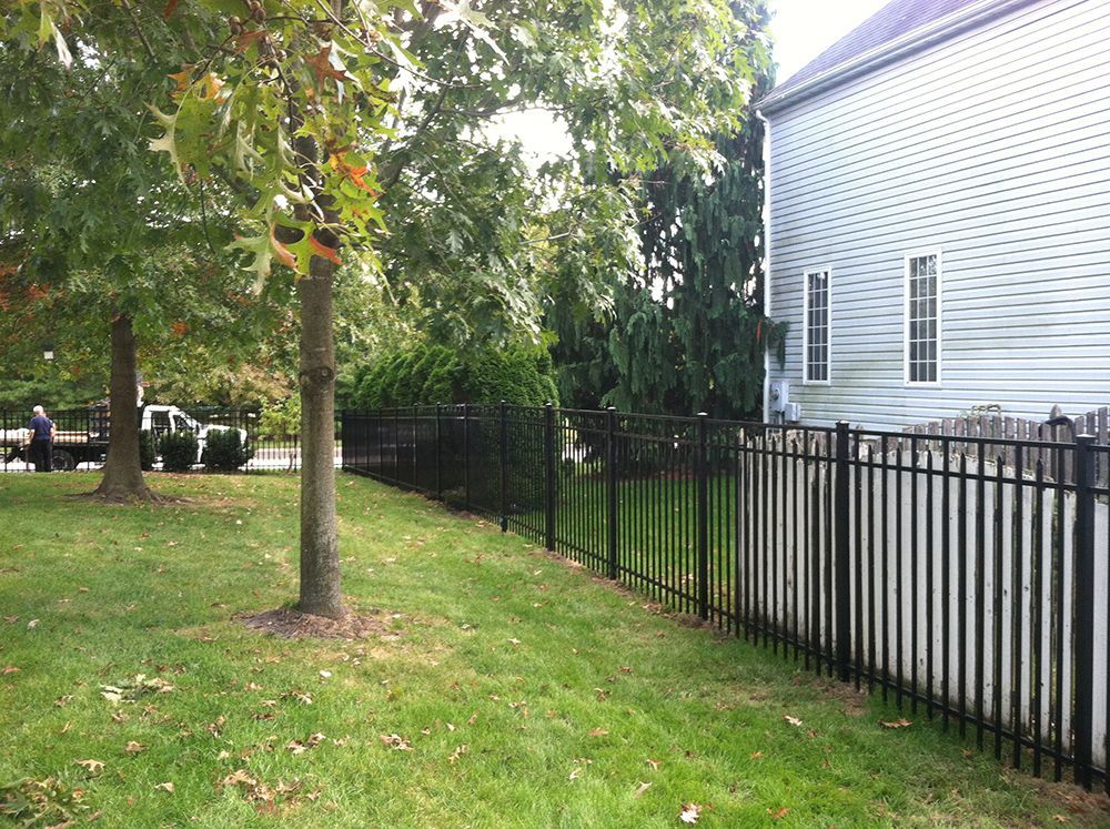 Black metal fence bordering a grassy lawn next to a two-story house with trees in the background.