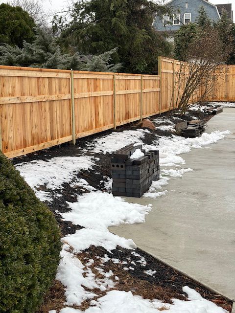 Wooden fence along a snowy edge with stacked gray cinder blocks.