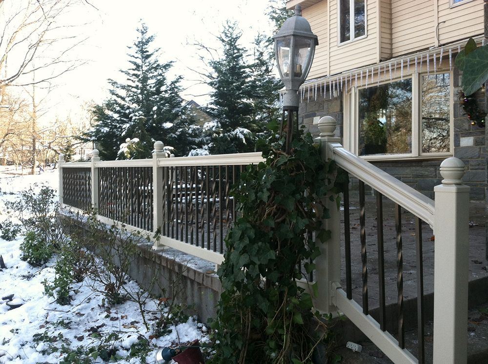 Snowy outdoor deck with white railing, black metal balusters, ivy, and a lamp post. House in the background.