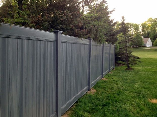 Gray vertical-plank fence bordering a grassy yard with trees in the background.