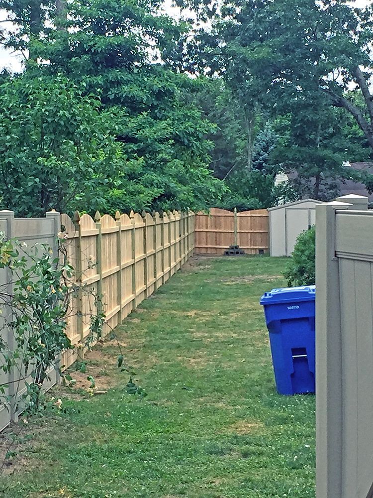 Backyard with wooden fence, green grass, and blue trash bin. Trees in the background.