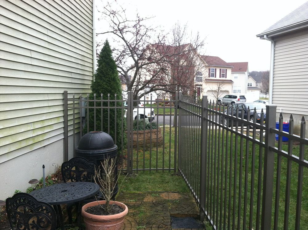 Metal fence bordering a grassy area next to a house with outdoor furniture. Overcast day.