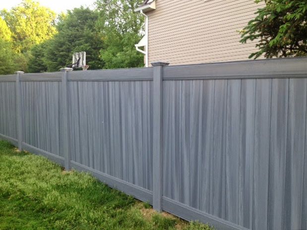 Gray vinyl privacy fence in a grassy yard, near a house and trees.