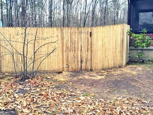 Wooden fence with gate in yard, surrounded by trees and leaves.