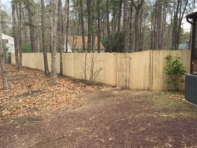 Bamboo fence in a wooded backyard setting with fallen leaves on the ground.