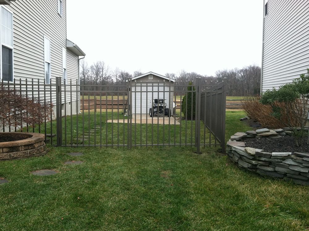 Backyard with a brown metal fence surrounding a shed between two houses.