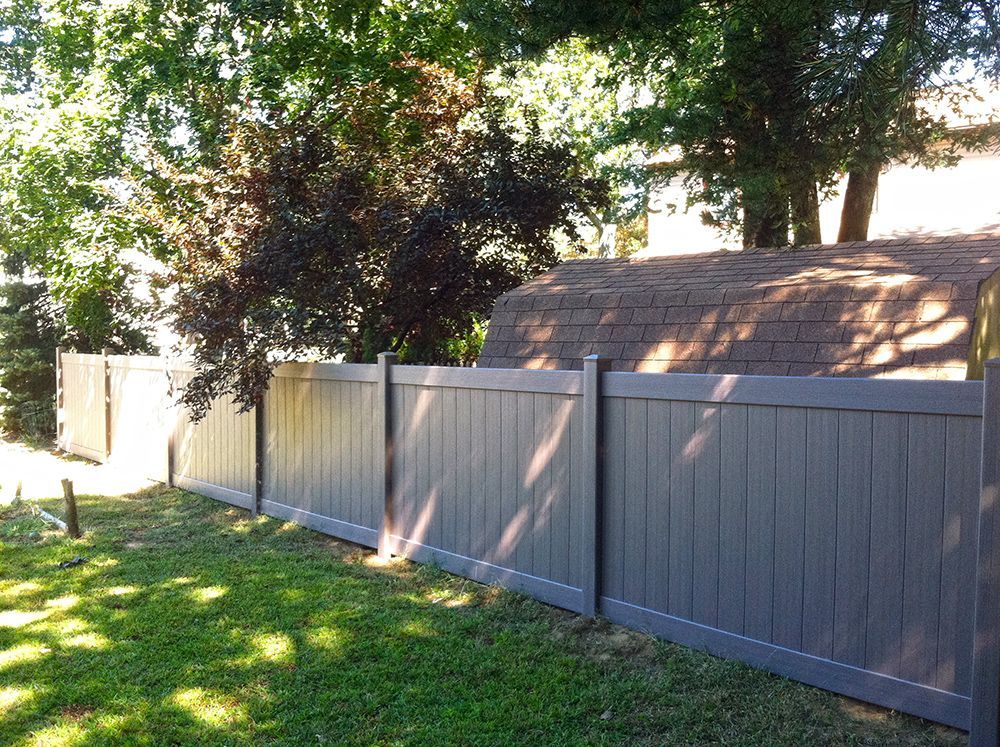 Gray vinyl fence in a backyard with trees and a shed.