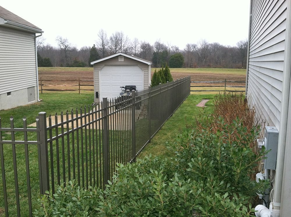 Metal fence in a backyard, separating a house and a garage from a field, on an overcast day.