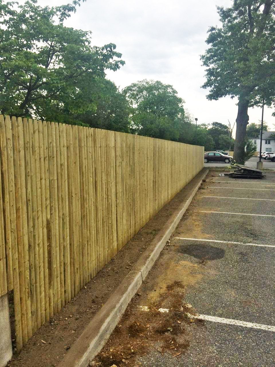 Wooden fence along a parking lot. Trees in the background.