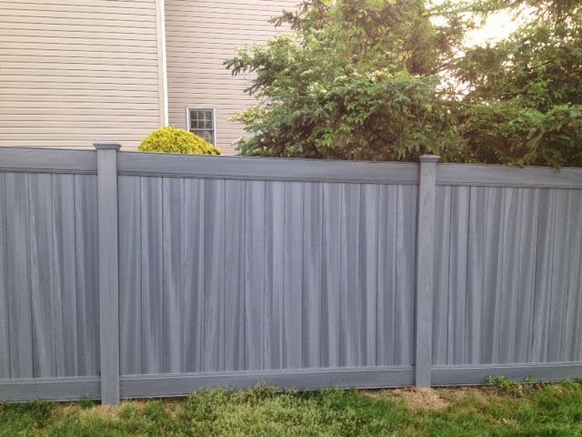 Gray vertical plank fence in a yard, with green grass and trees in the background.