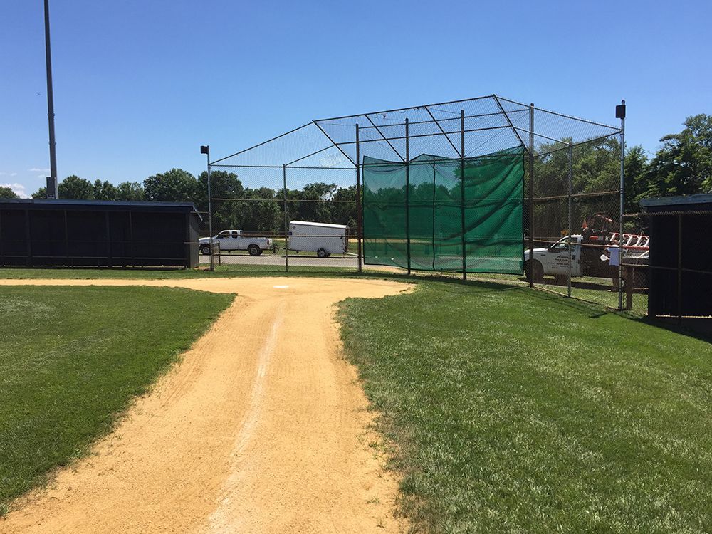 Dirt path leading to baseball batting cages, set on a grassy field, under a blue sky.