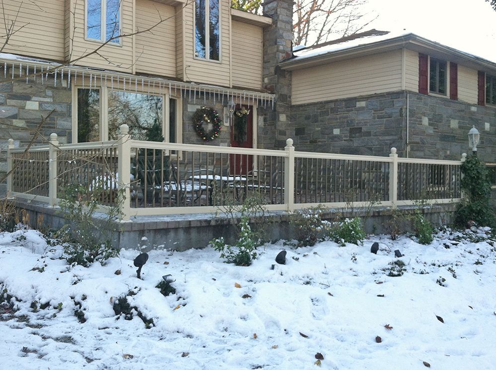 Snowy outdoor deck with cream-colored railing, stone house exterior, small plants, and icicles.