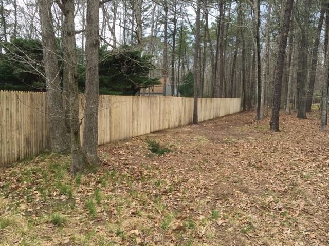 Wooden fence bordering a wooded area with bare trees and fallen leaves.