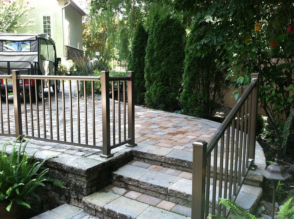 Stone steps lead to a brick patio with brown metal railings. A van is parked nearby.