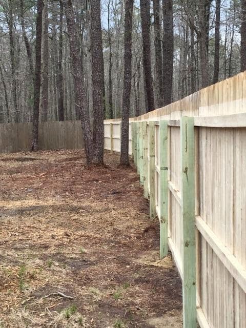 Wooden fence in a wooded area with trees and brown foliage.