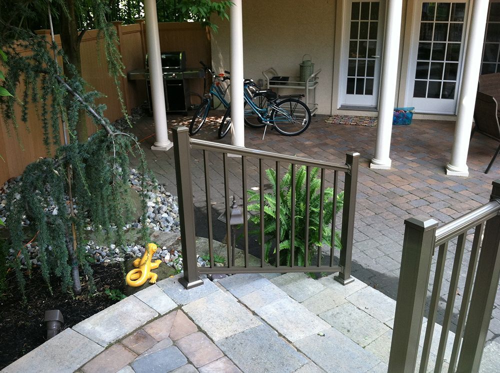 Bronze railing on stone steps, leading to a patio with white columns and a bicycle.