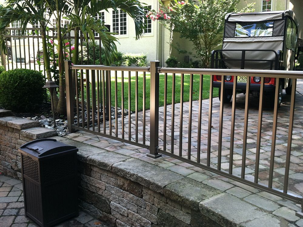 Metal fence atop stone wall near a golf cart and building with palm trees.