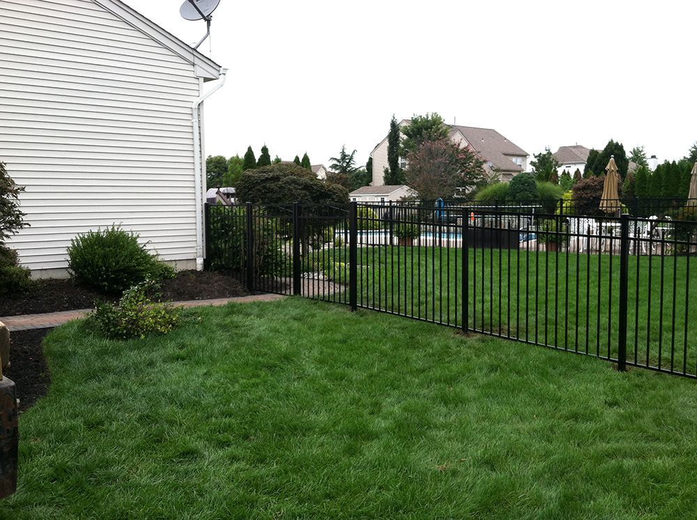 Black metal fence bordering a green lawn next to a white house.