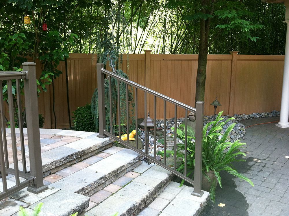 Stone steps with a brown railing and fence, leading to a patio. Ferns and bamboo visible.