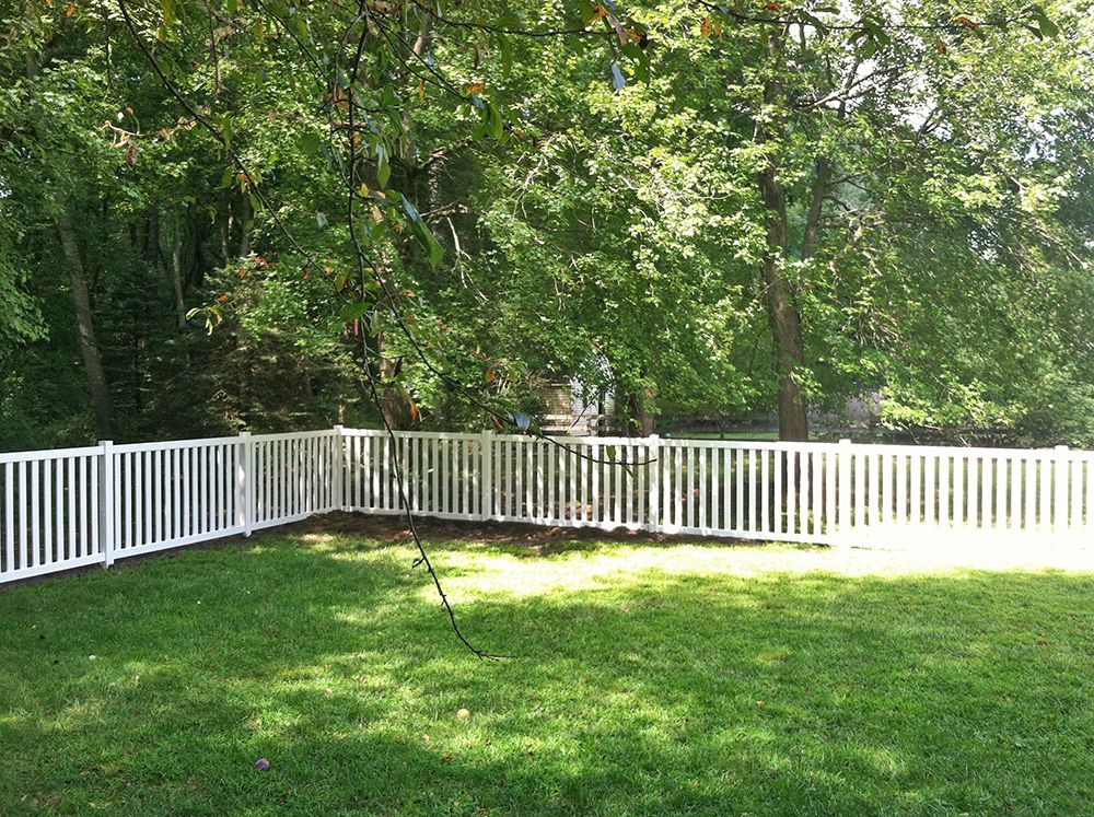 White picket fence enclosing a grassy backyard, surrounded by trees.