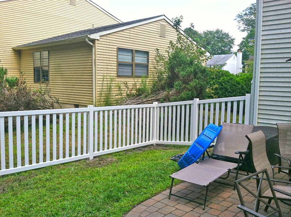 White picket fence in a grassy backyard with patio furniture and a house in the background.