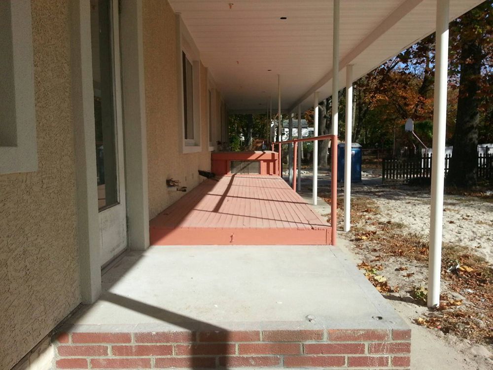 Long, covered porch with brick steps, red deck, and beige siding.