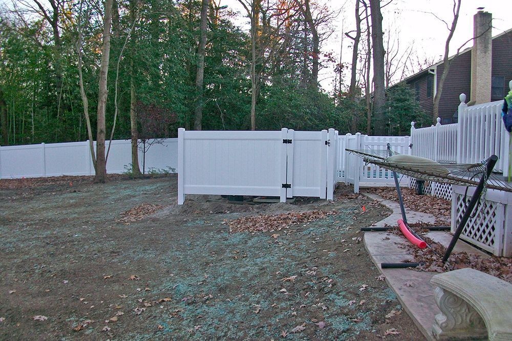 White fenced backyard with a gate, trees, and ground covered in seed.