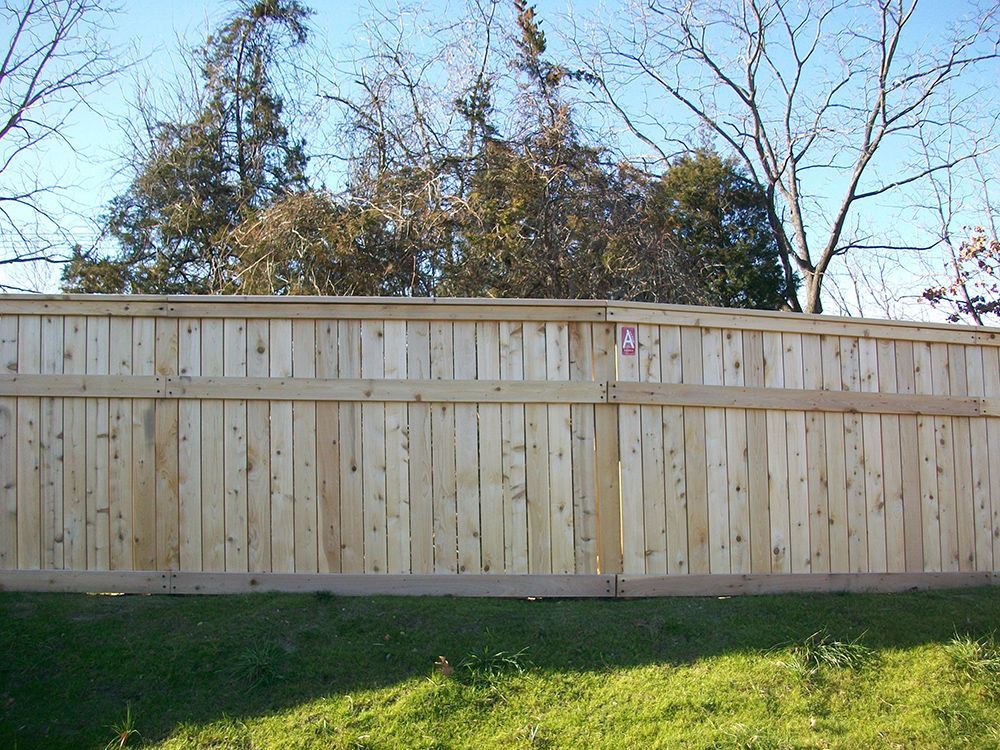 Wooden privacy fence in front of green grass and trees.