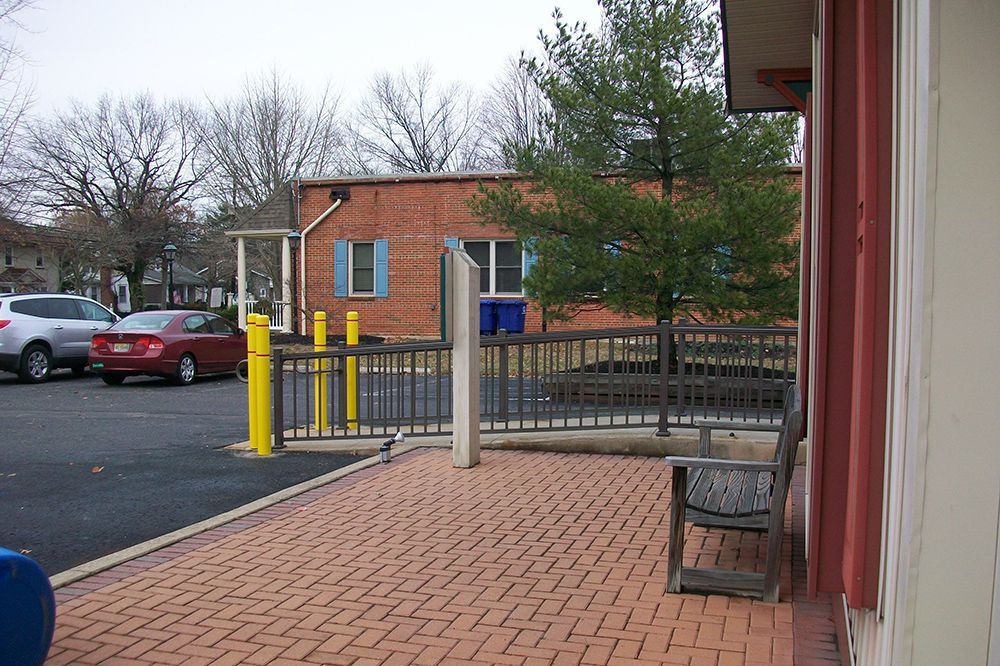 Brick patio with a metal fence, red brick building, parked cars, and a tree.