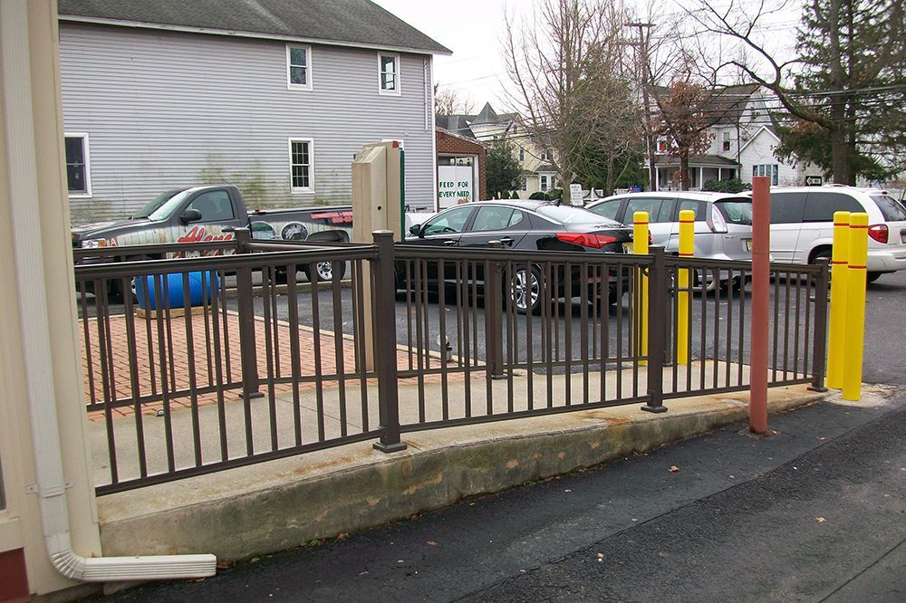 Metal railing separating a parking area from an adjacent building; vehicles in the parking lot.