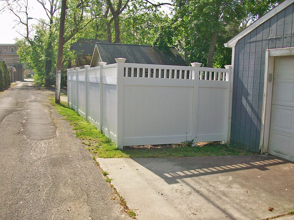 White vinyl fence next to a paved alley, beside a gray garage.