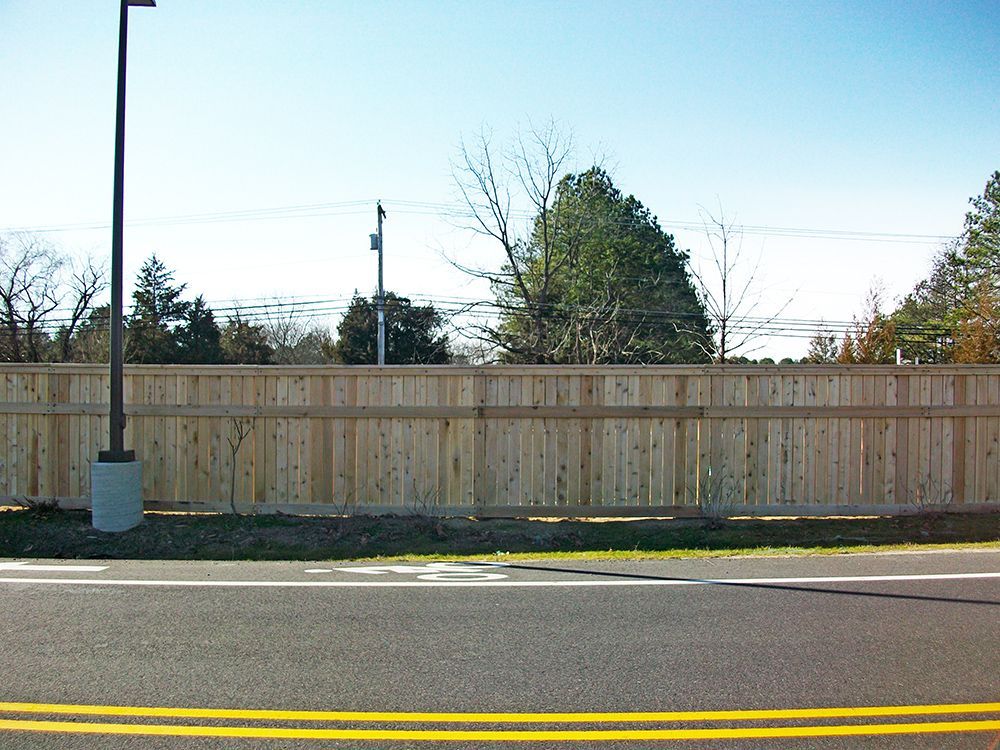 A wooden fence bordering a road under a blue sky, with a street lamp.