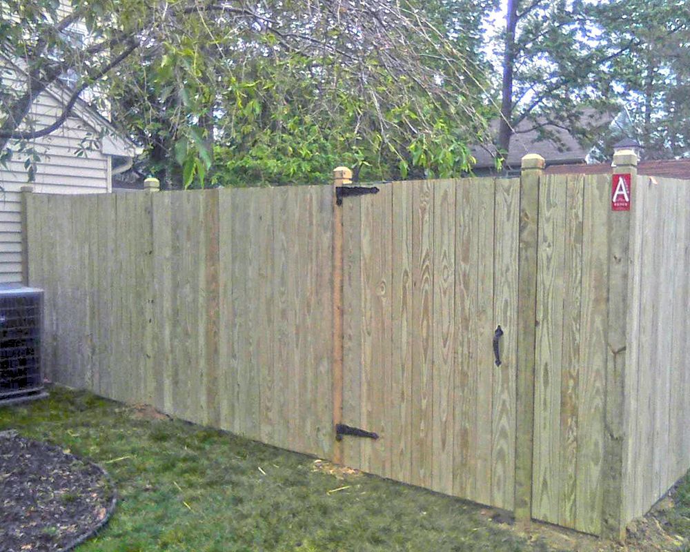 Wooden fence with gate in a backyard, featuring a small air conditioning unit.