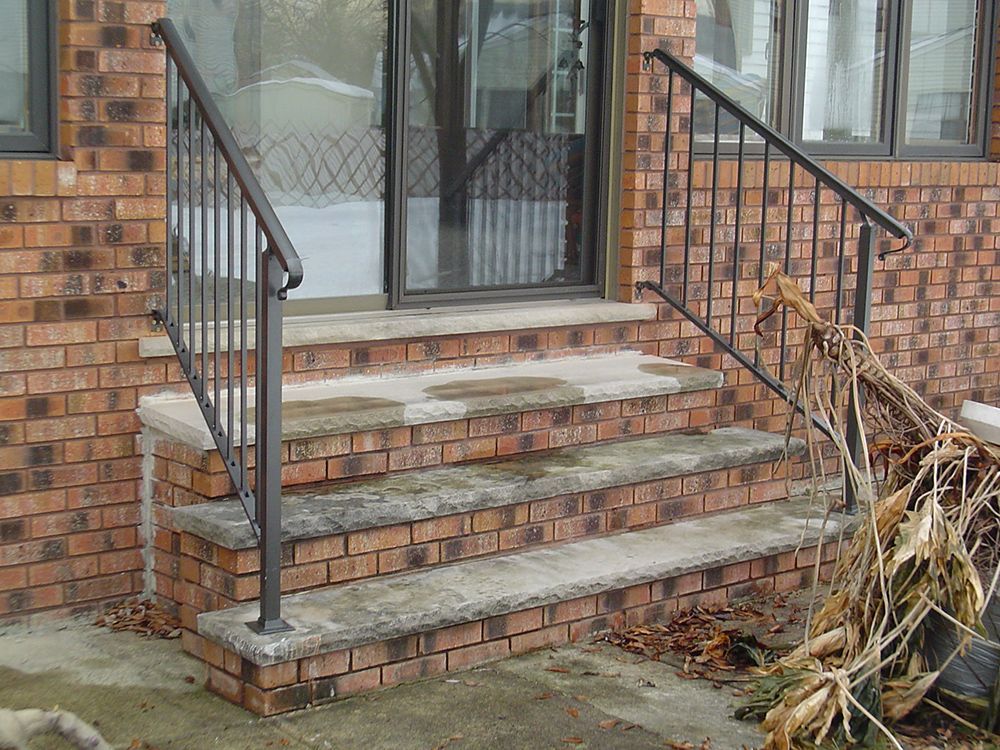 Brick steps leading to a door with black handrails on either side.