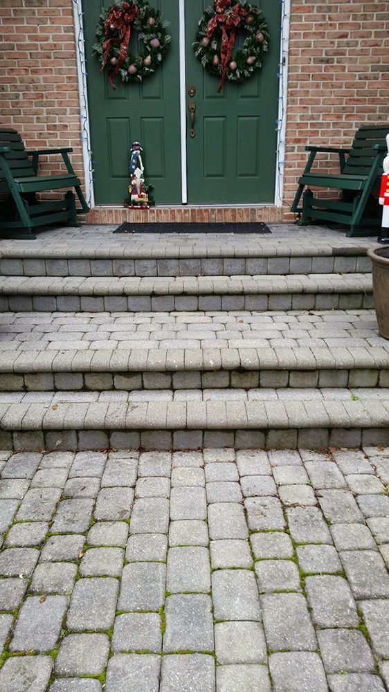 Stone steps leading to a green door with Christmas wreaths. Two green chairs sit on the porch.