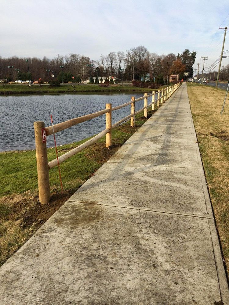 Concrete path beside a pond, with a wooden split-rail fence alongside the water.