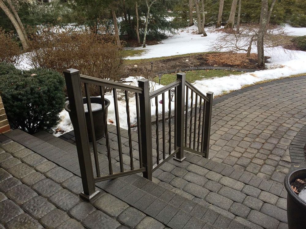 Stairs with dark railing on a brick patio, snow in the background.