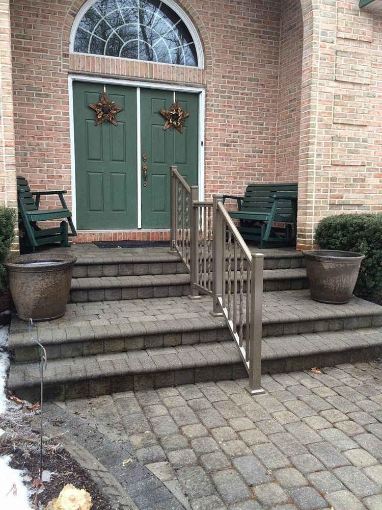 Exterior of a brick home with green double doors, steps, and brown planters. Two green benches are on the porch.