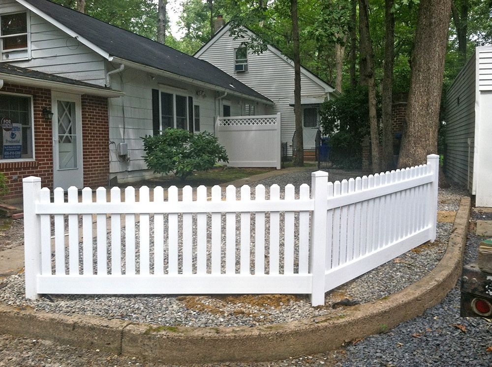 White picket fence curving around a gravel area next to a house with a dark roof.