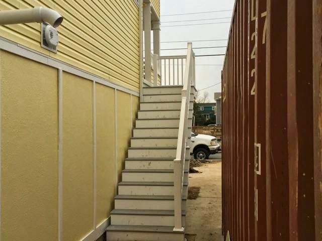 Wooden staircase next to a yellow building and brown container; outdoor setting.