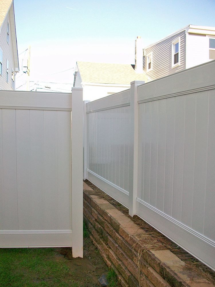 White vinyl fence bordering a narrow passageway with a low brick retaining wall.