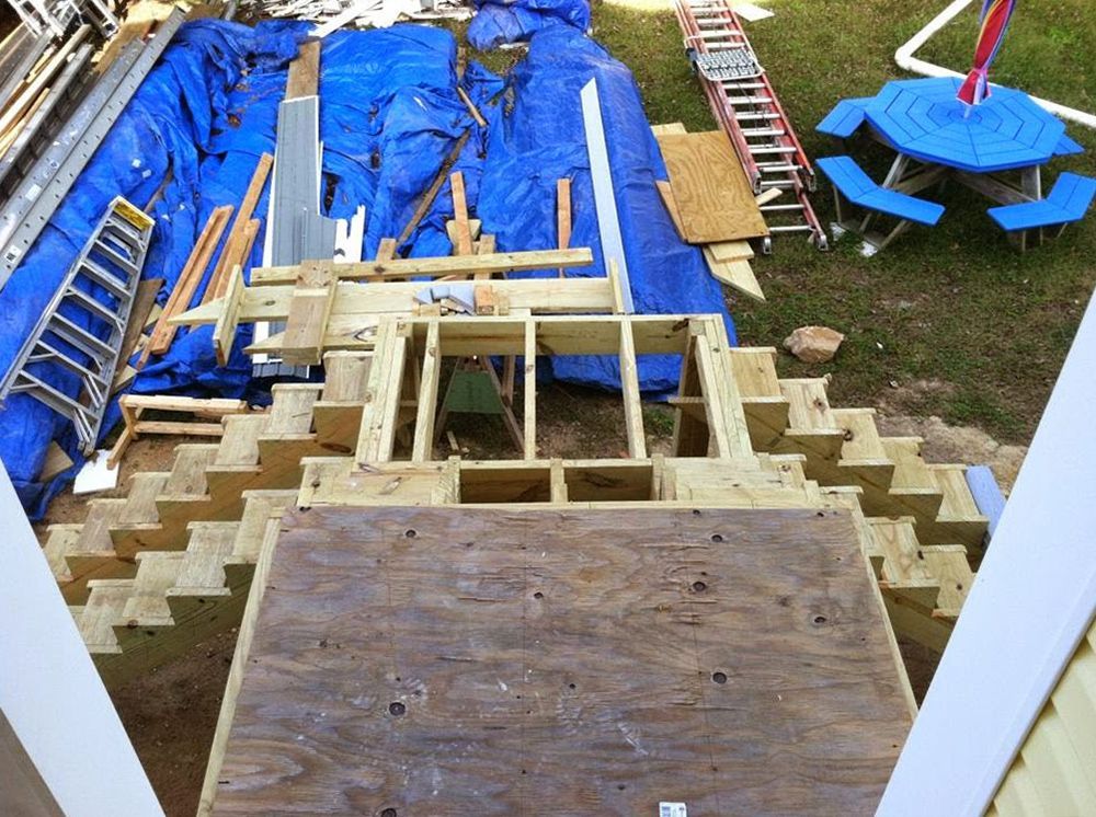 Wooden staircase under construction, framed against blue tarp and lawn.