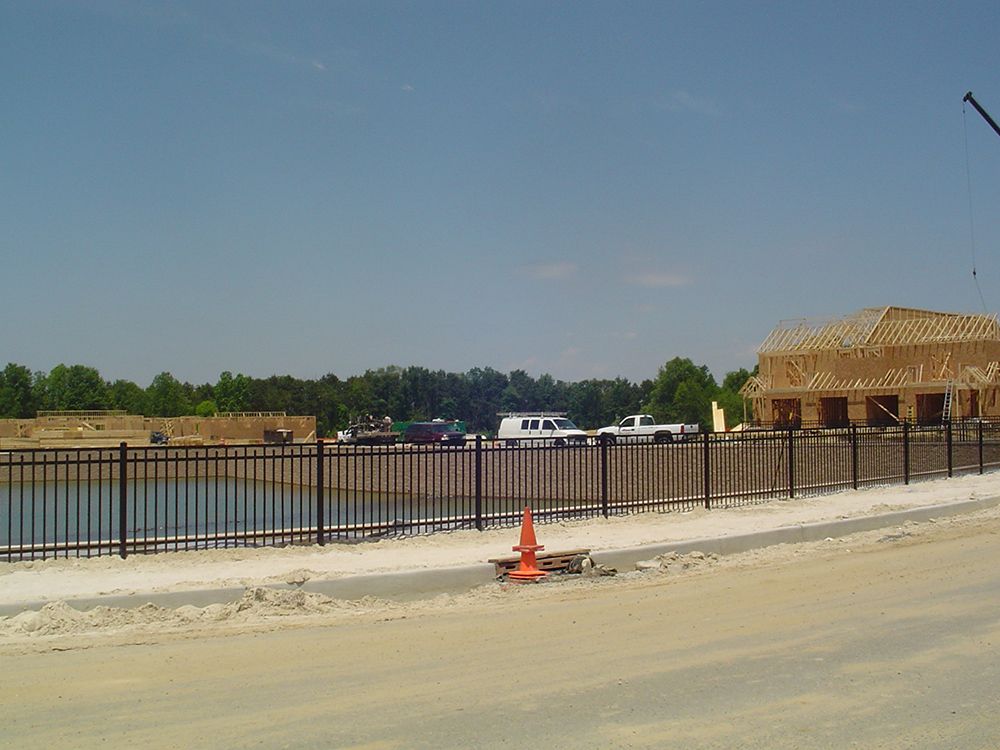 Construction site with a lake, black fence, partially built building, and blue sky.