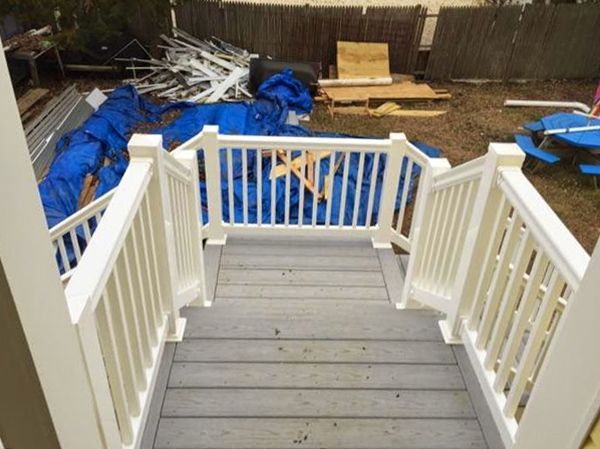 White-railed stairs leading down to a backyard with debris covered by blue tarps.