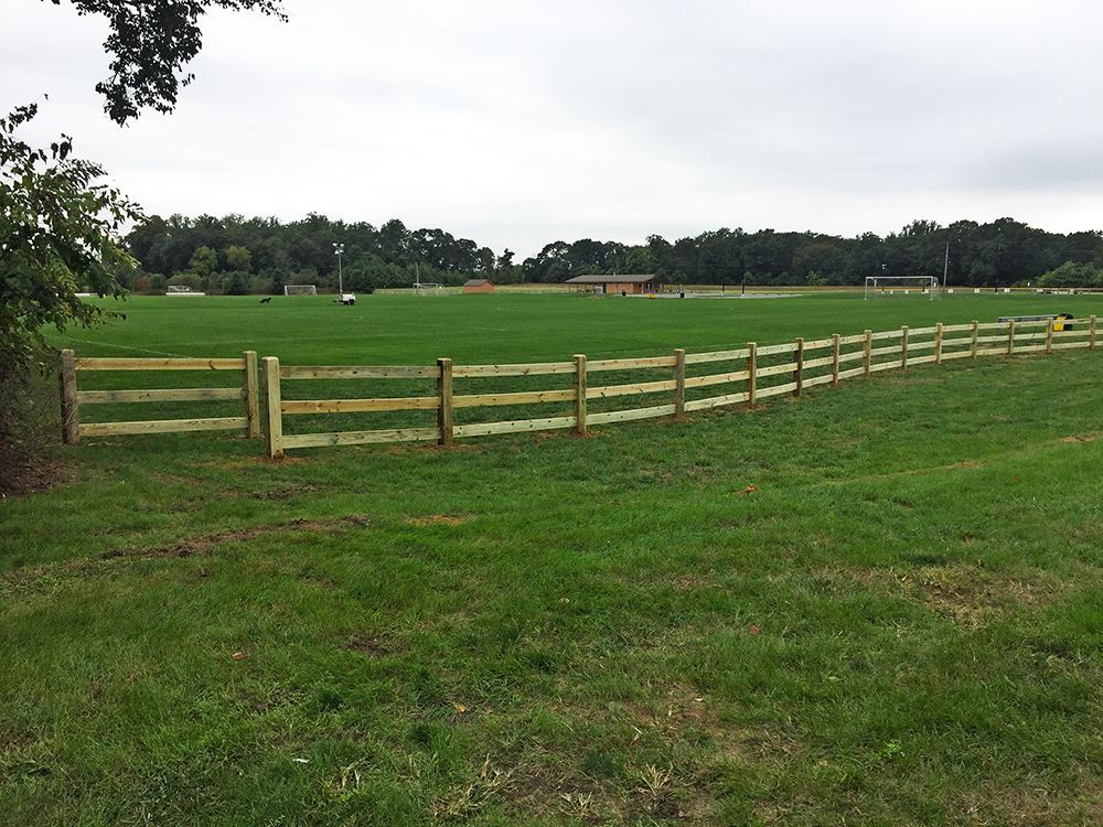 Wooden fence around a grassy field under a cloudy sky.